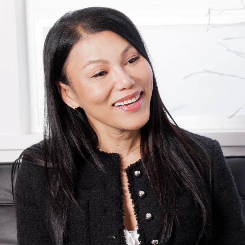 Smiling woman with long black hair wearing a black jacket in a bright indoor care setting