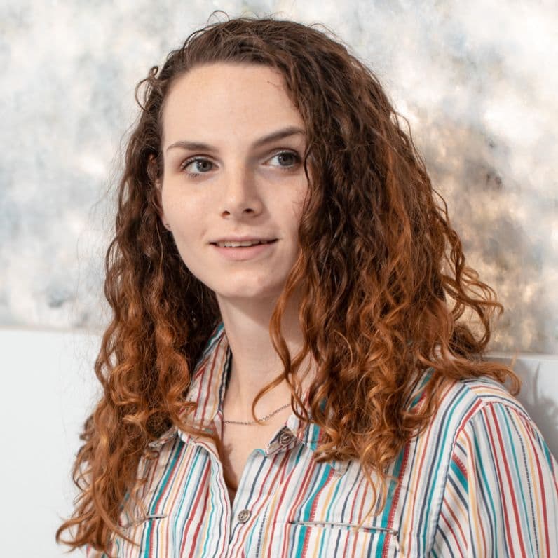 Portrait of a young woman with curly red hair wearing a striped shirt in a bright care setting