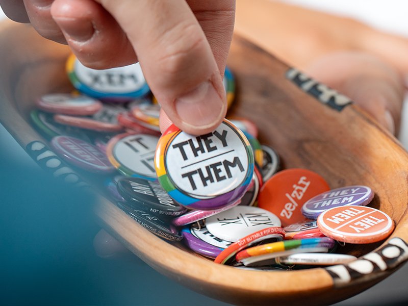 Close-up photo of LGBT-themed buttons, including one saying They/Them