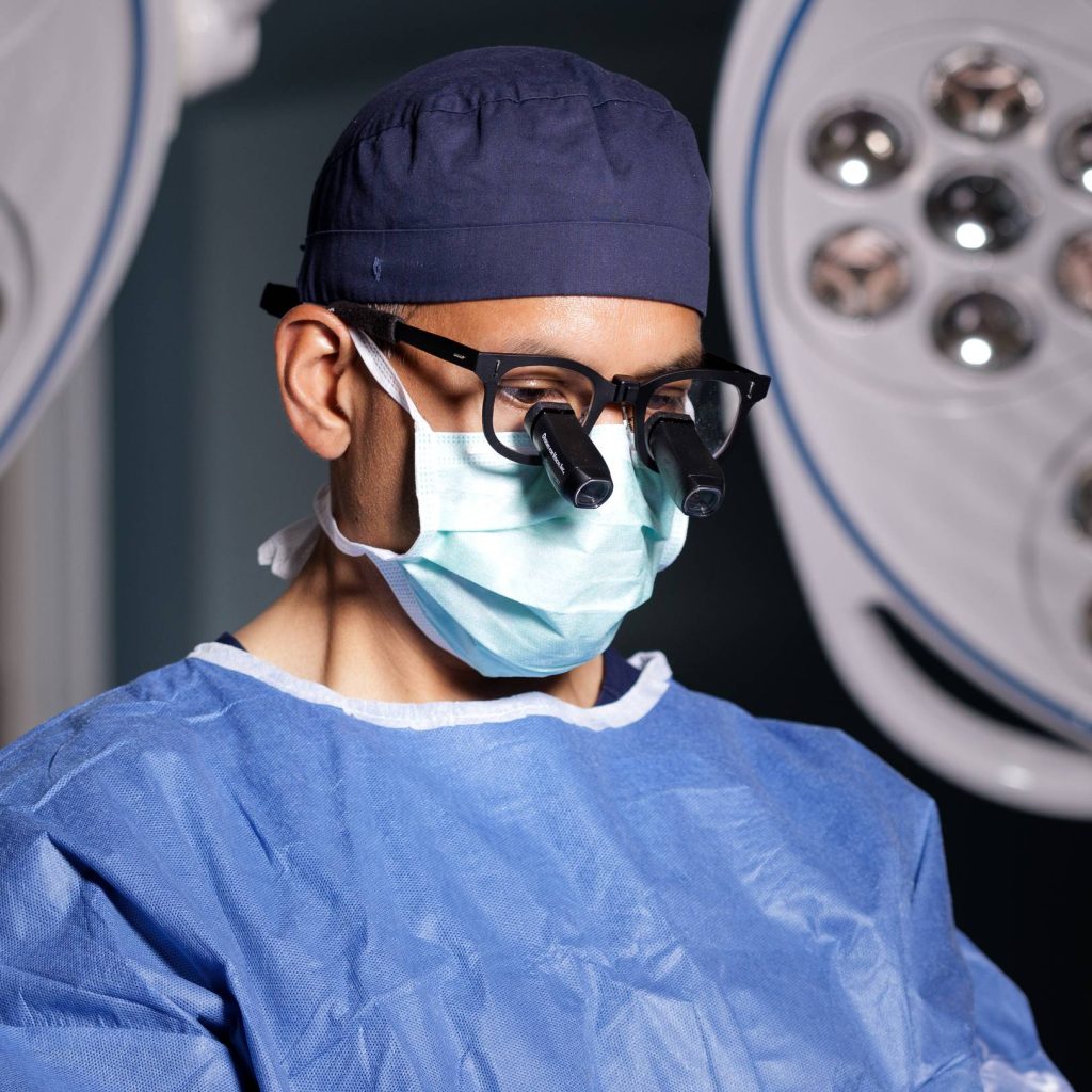 Dr. Gurjala wearing surgical loupes and mask in an operating room
