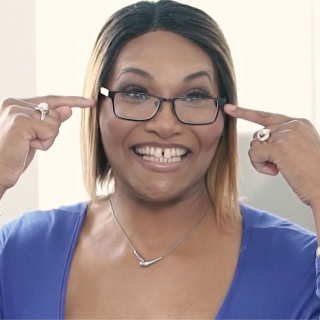 Smiling woman in glasses pointing to her eyewear.
