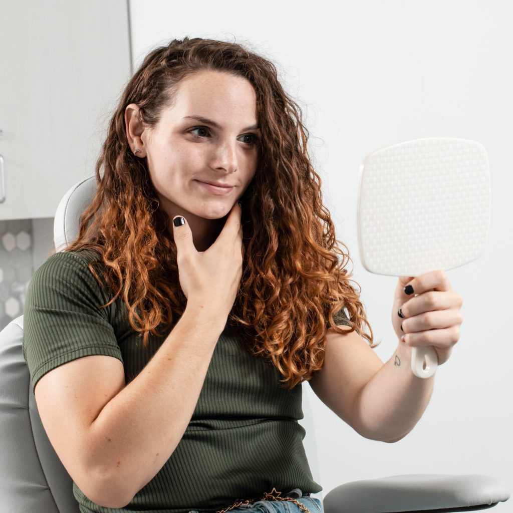 Patient holding a hand mirror while sitting in a medical exam chair.